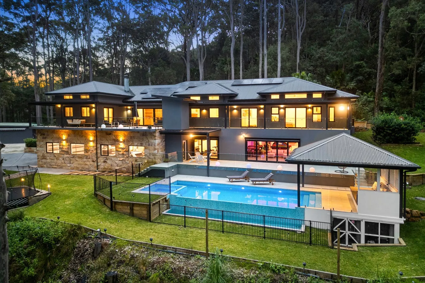 Two-storey Bayview home in bushland at dusk with the pool in the foreground