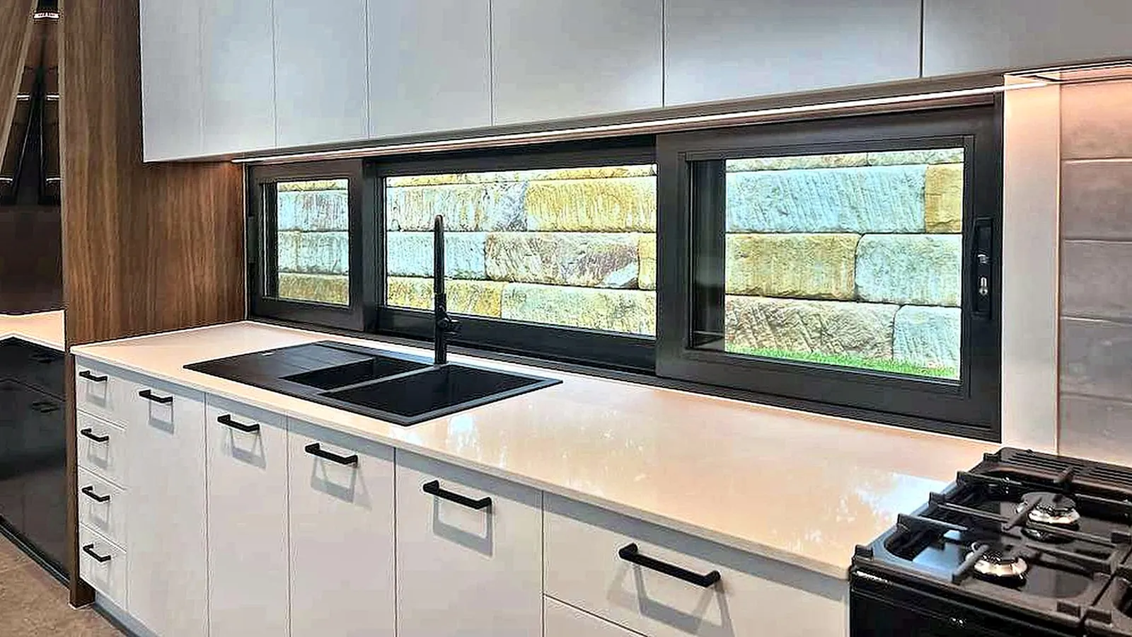 Full-width kitchen window framing a sandstone retaining wall
